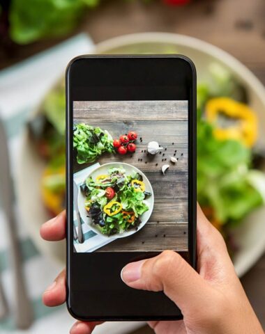 food blogger holding phone over plate of salad